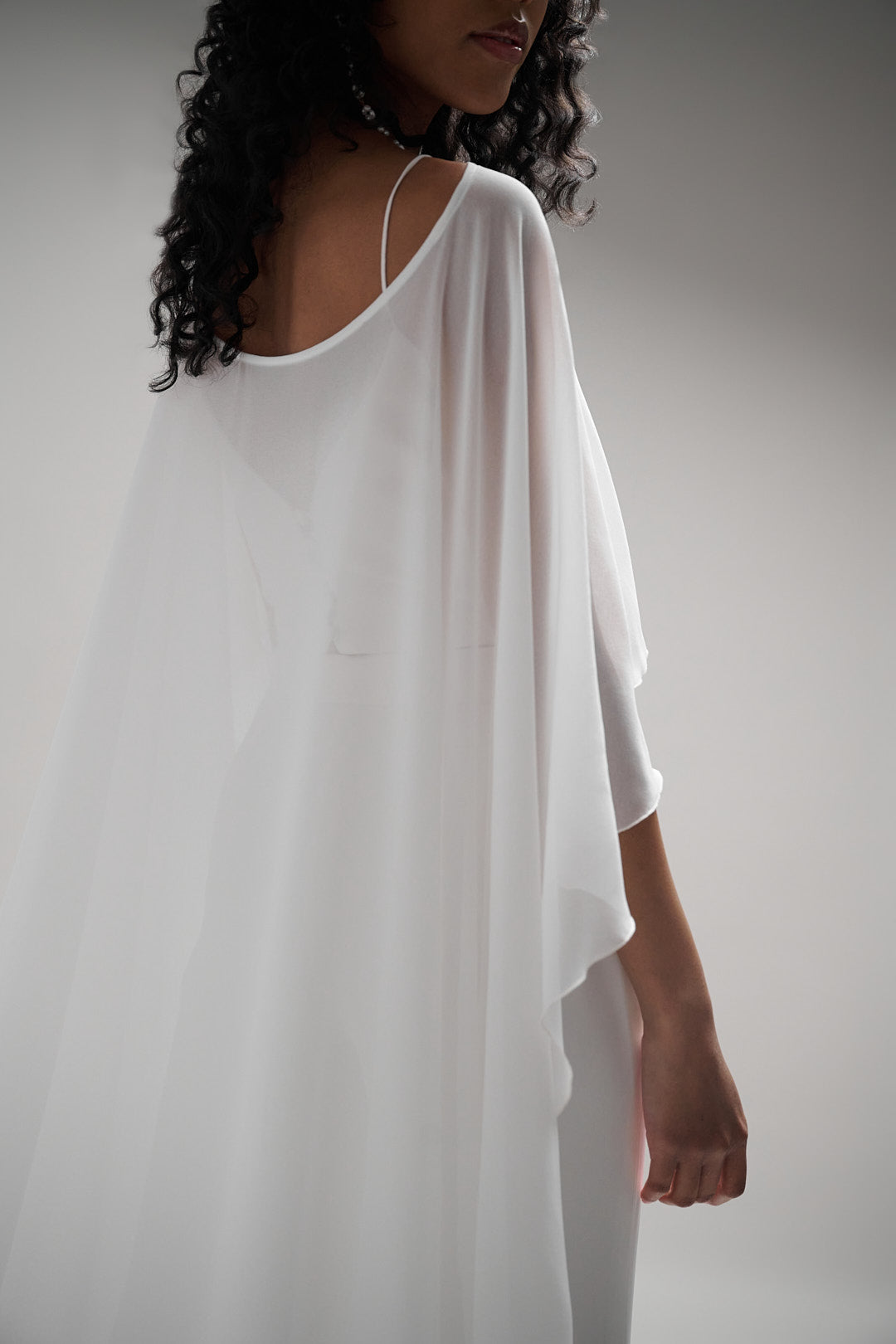 A model wears the Beatrix Cape, a chiffon cape that offers dramatic flair for the fearless bride. The cape is a perfect veil alternative for those with bold style and editorial tastes, with its light, airy fabric that moves with you to create an air of whimsical elegance