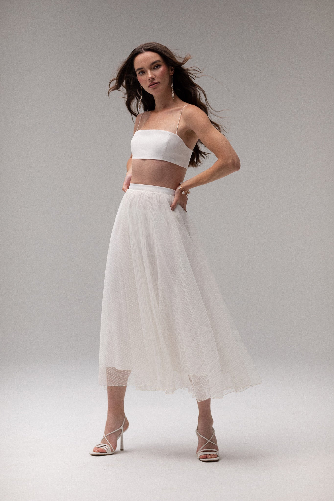 Model wearing a pleated tulle skirt overlay from the J'OSE Collection by TEMPÊTE, featuring a sheer, flowing design perfect for layering over bridal outfits.