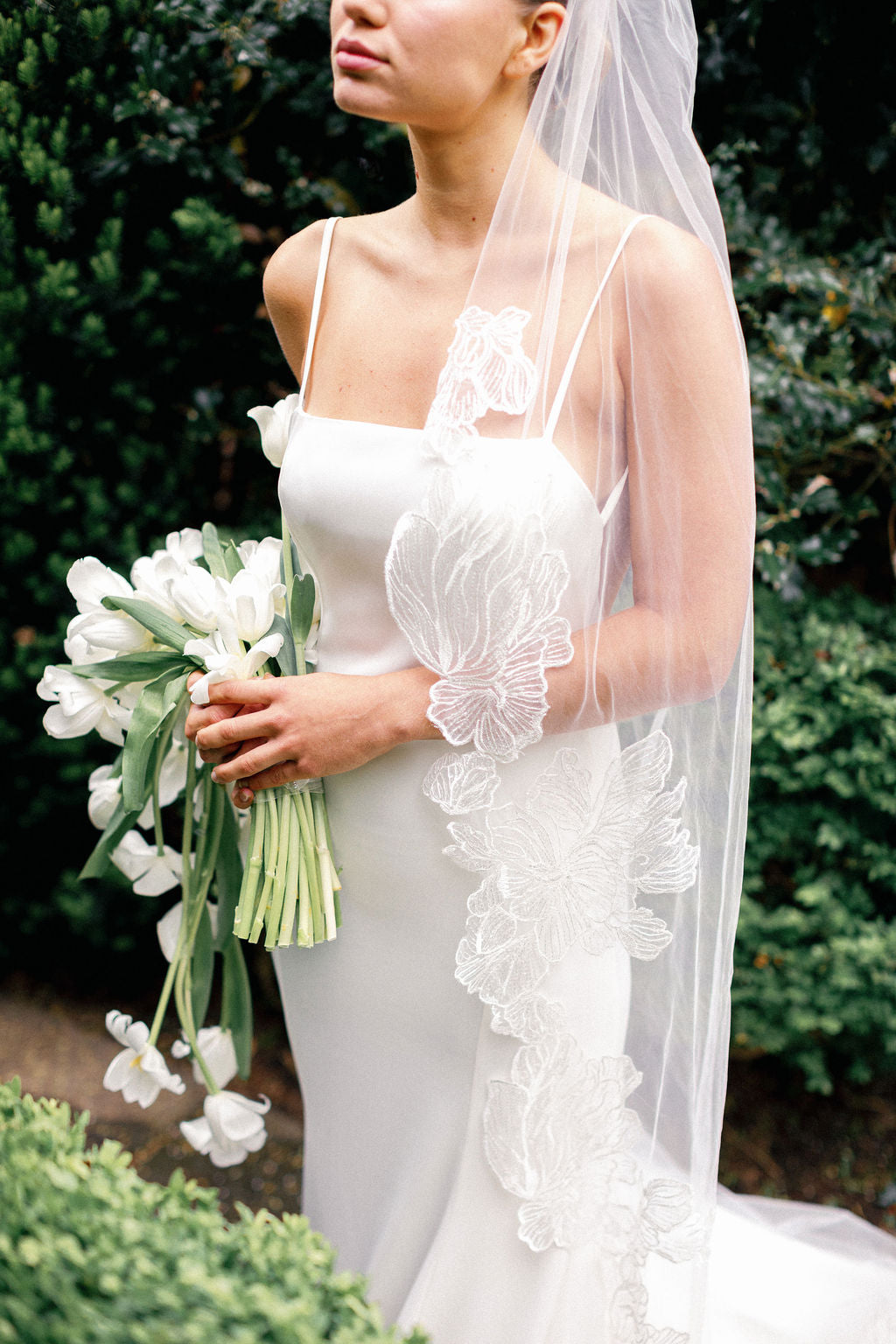 Bride in a white wedding dress with a floral veil holding a bouquet of white tulips.